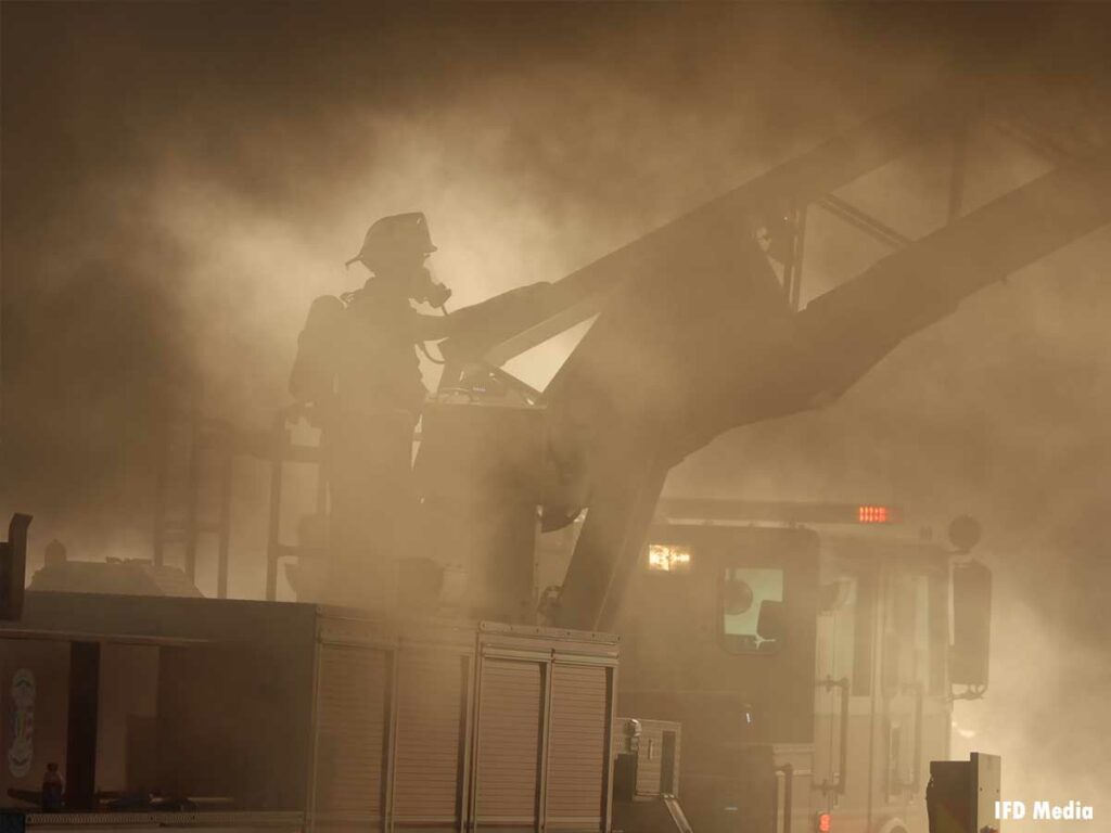 A firefighter in full gear on a turntable in the smoke