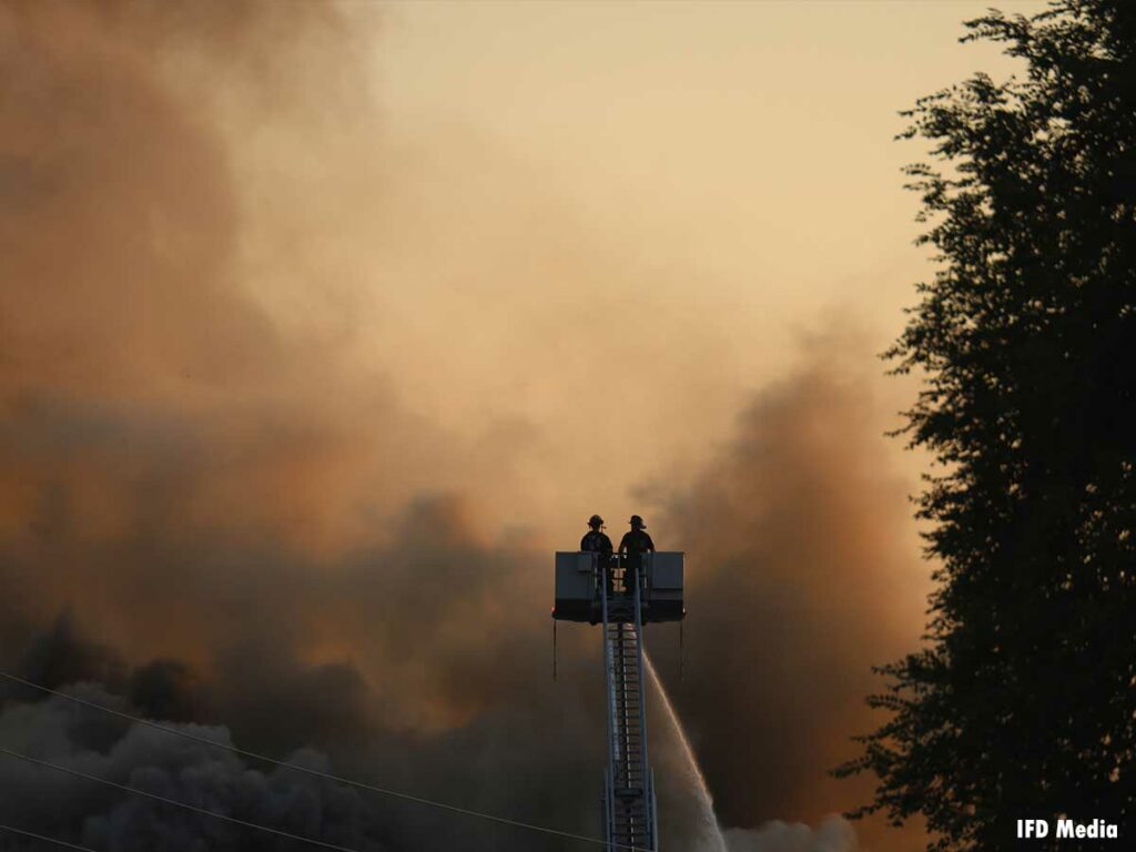 Two firefighters in a tower ladder bucket with an elevated stream