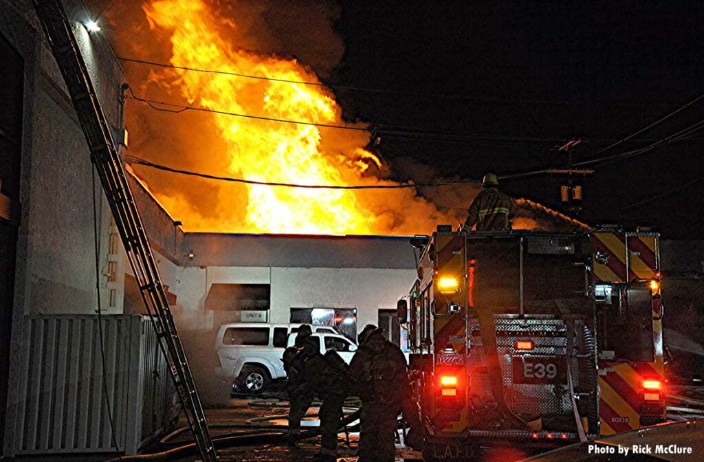 LAFD firefighters with major flames shooting through roof of fire building