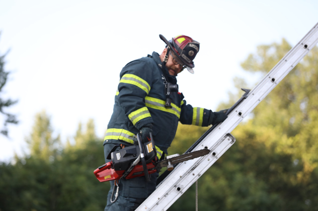 A firefighter in turnout gear stands on a latter.