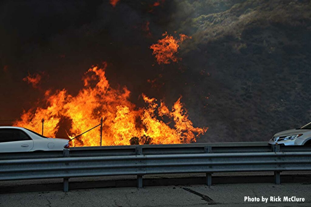 Cars drive past wildfire flames