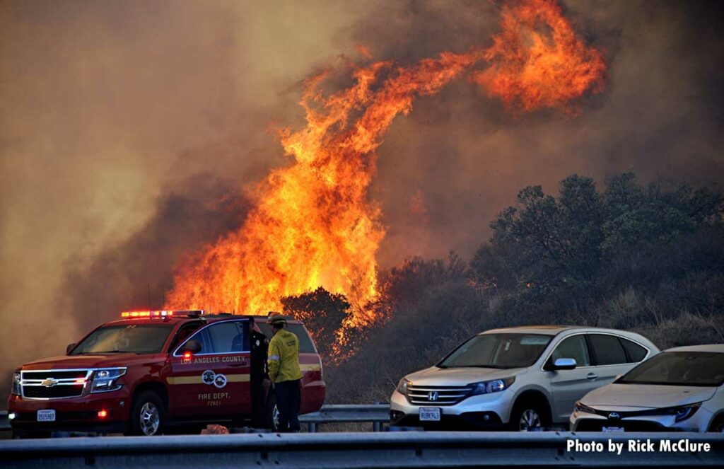 Firefighter near Los Angeles County chief's SUV as flames roar behind roadway