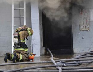 Firefighter masks up outside a door with smoke showing