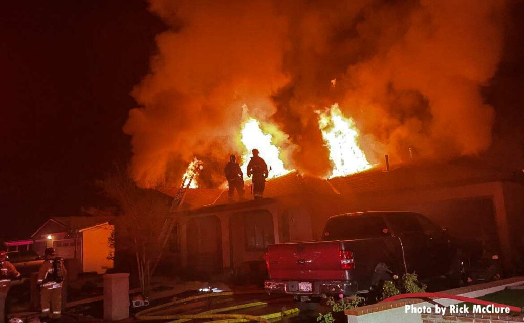 Ladder set up at house fire with firefighters making the roof