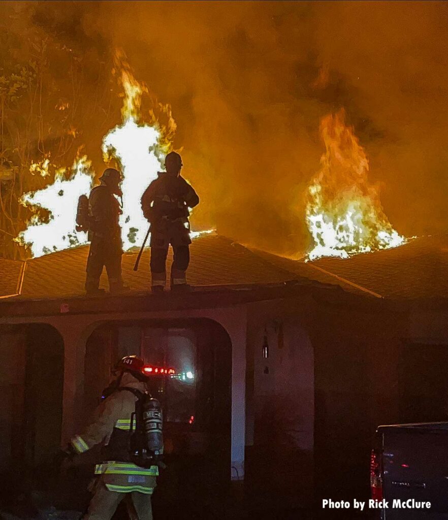 Flames as firefighters operate on the roof of a home