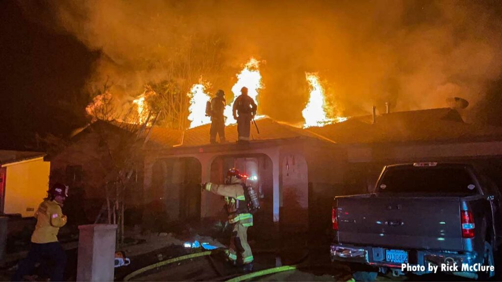 Firefighters with flames shooting through roof at fire scene