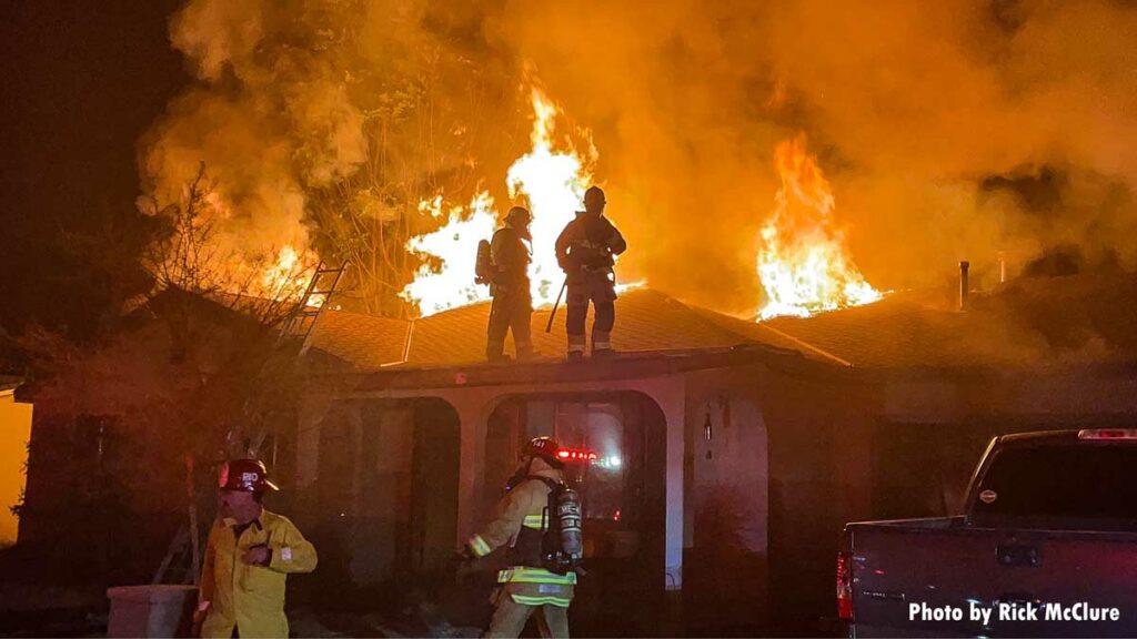 Two firefighters on roof with flames