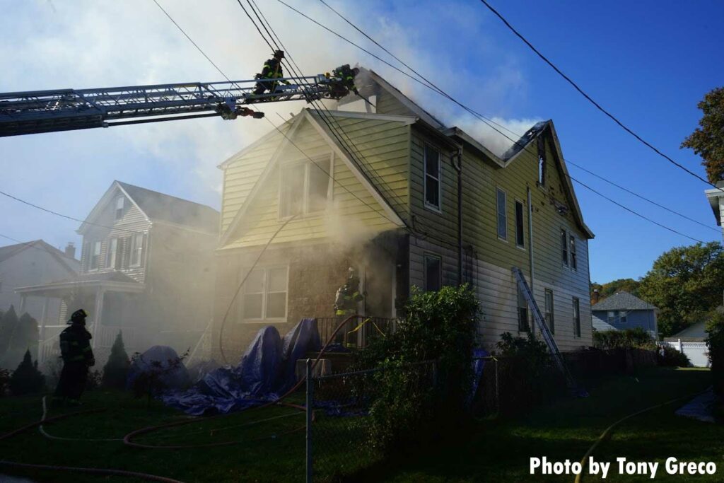 Firefighters on an aerial and working on the fire building with a hoseline out the window