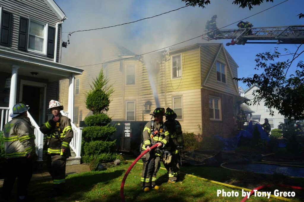 Firefighters on an aerial ladder while other firefighters hold a hose