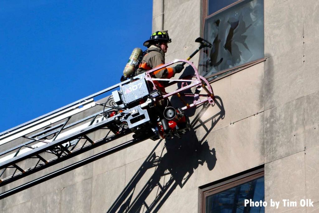 From aerial ladder, firefighter uses ax to break window of building