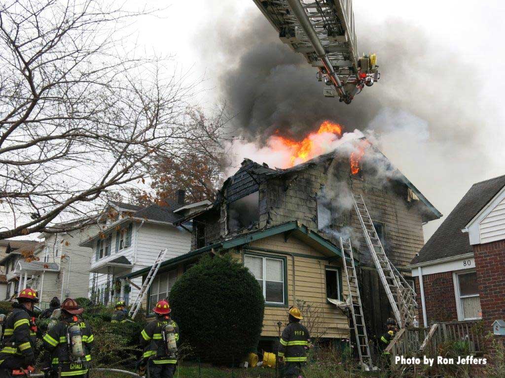 Aerial ladder and firefighter with flames belching from roof