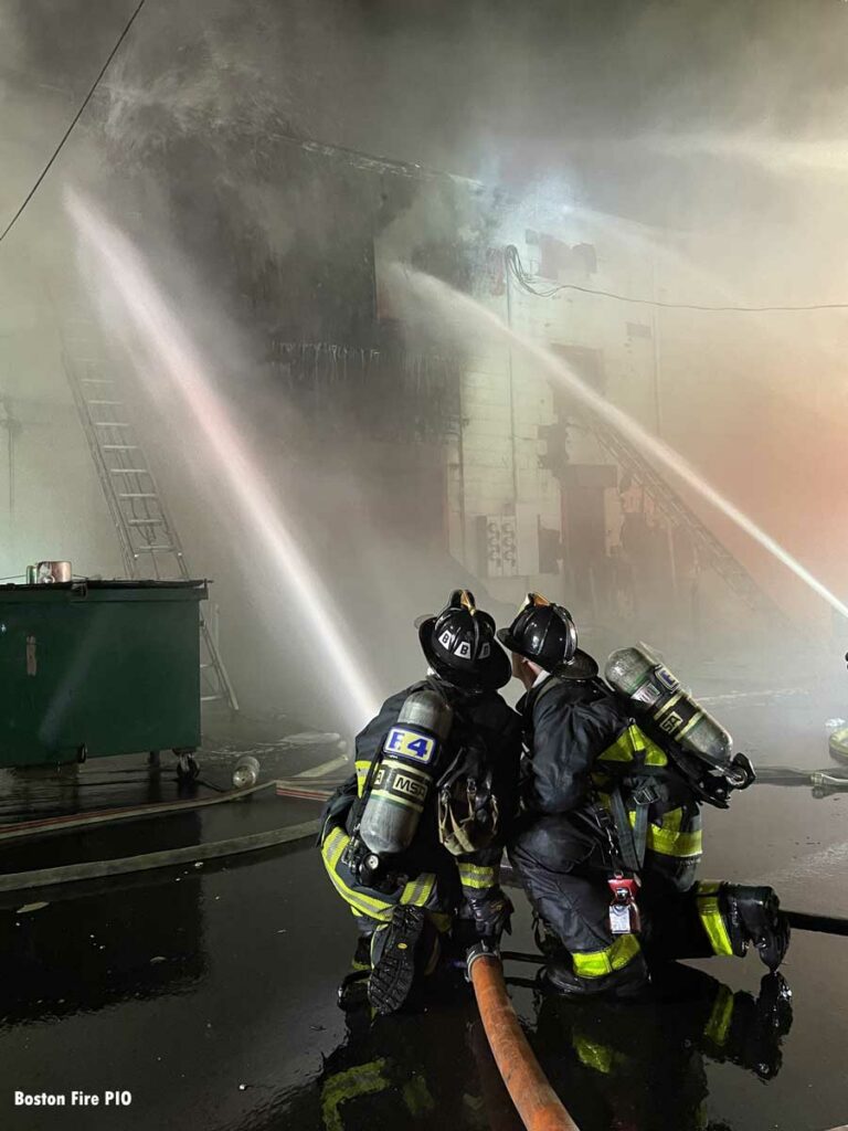 Two firefighters kneel on a hoseline at Boston fire