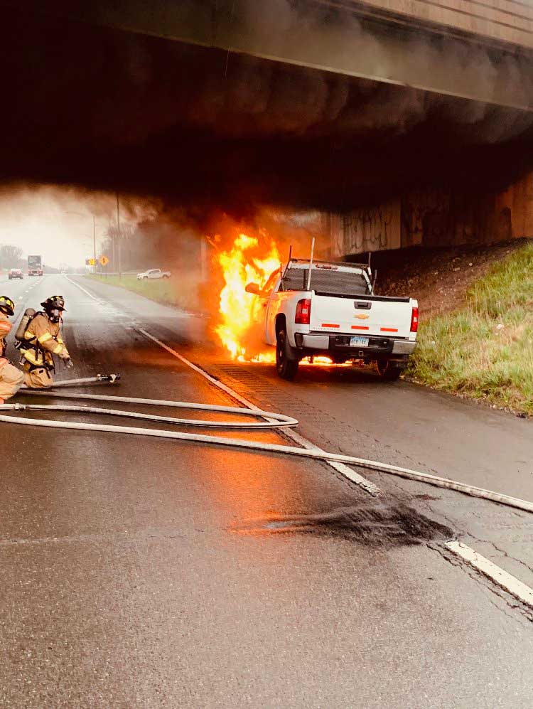 Flames shoot from pickup as firefighters ready a hoseline