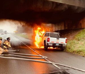 Firefighters with hoseline fight vehicle fire under bridge