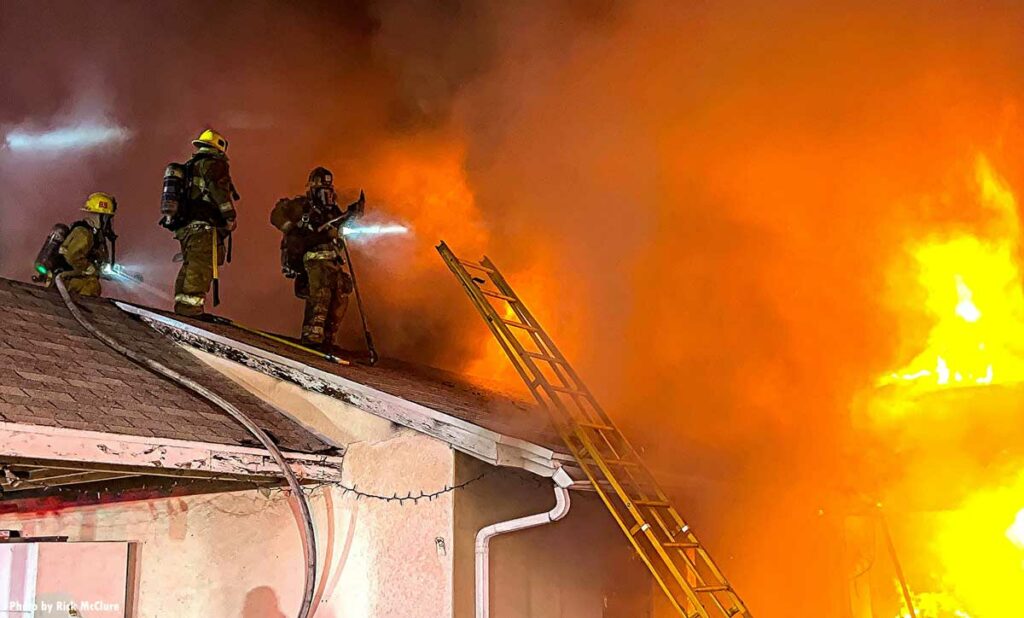 Three firefighters with hoseline on roof at house fire