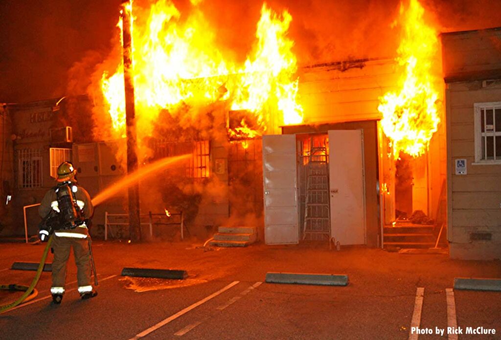 Firefighter with hoseline and fire showing from multiple points of building