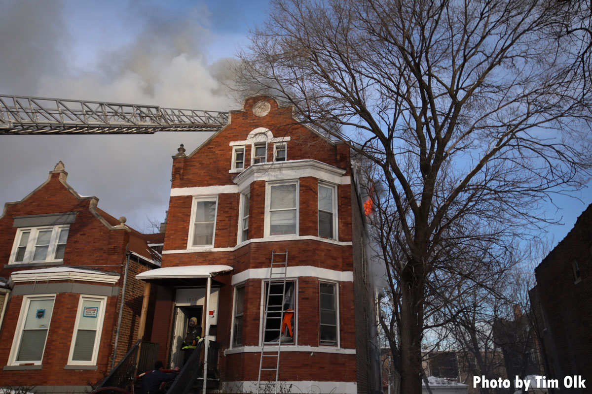 Flames out the second floor of a building with aerial ladder and portable ladder