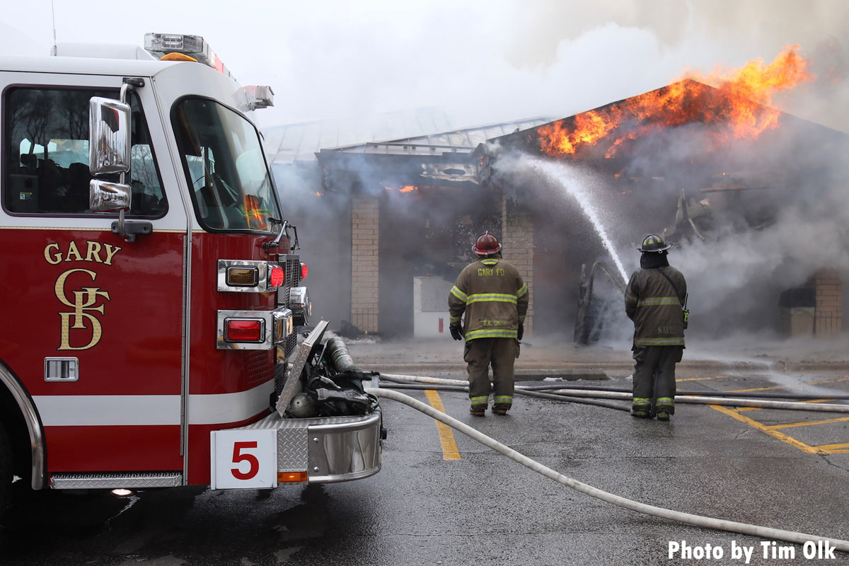 Gary IN fire trucka nd firefighters with hoseline fire through roof of building