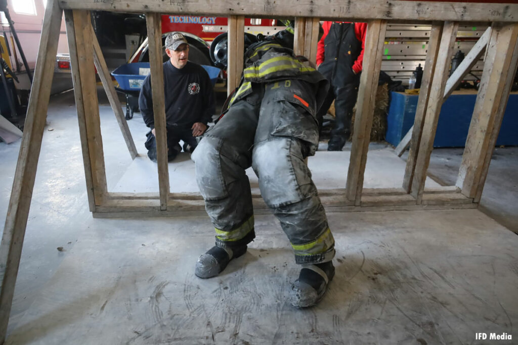 A firefighter twists to get between wall studs