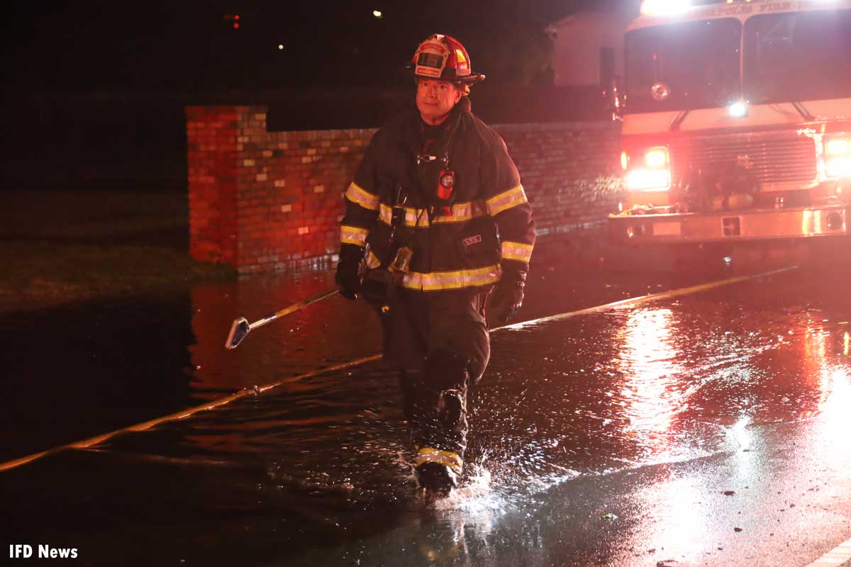 Firefighter walks through puddle with hook