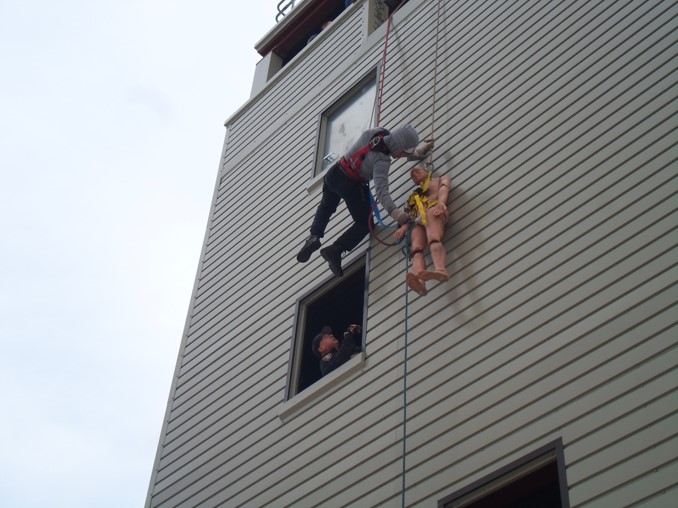 Firefighter rappelling with victim at training building