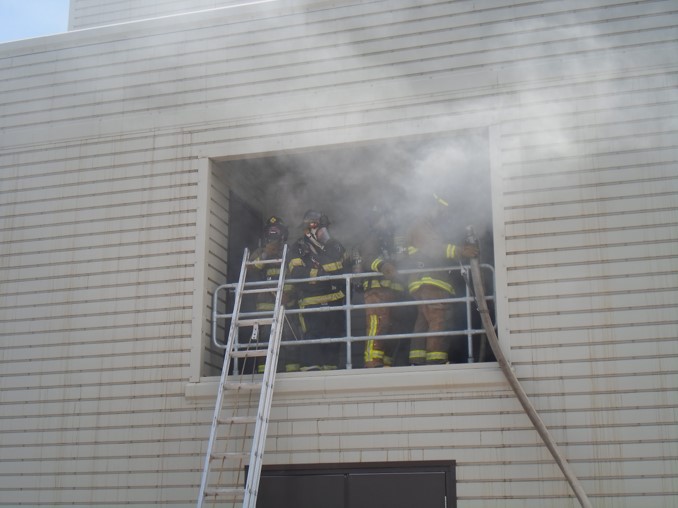 Firefighters with ladder and hoseline on balcony of burn building