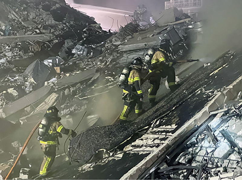 Firefighters stretched hundreds of feet of three-inch hose to supply handlines. In the background, a tower ladder operated its elevated master streams.