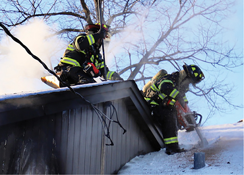 A member cuts the roof over the garage. Members exercise extreme care because of the snow and ice conditions. You can also see the impact of the heat on the eaves of the main structure, necessitating opening up an inspection hole in the main house roof.