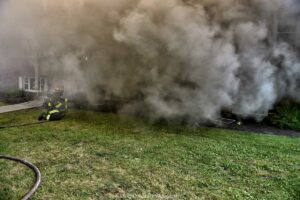 Firefighter on hoseline with smoke issuing from building