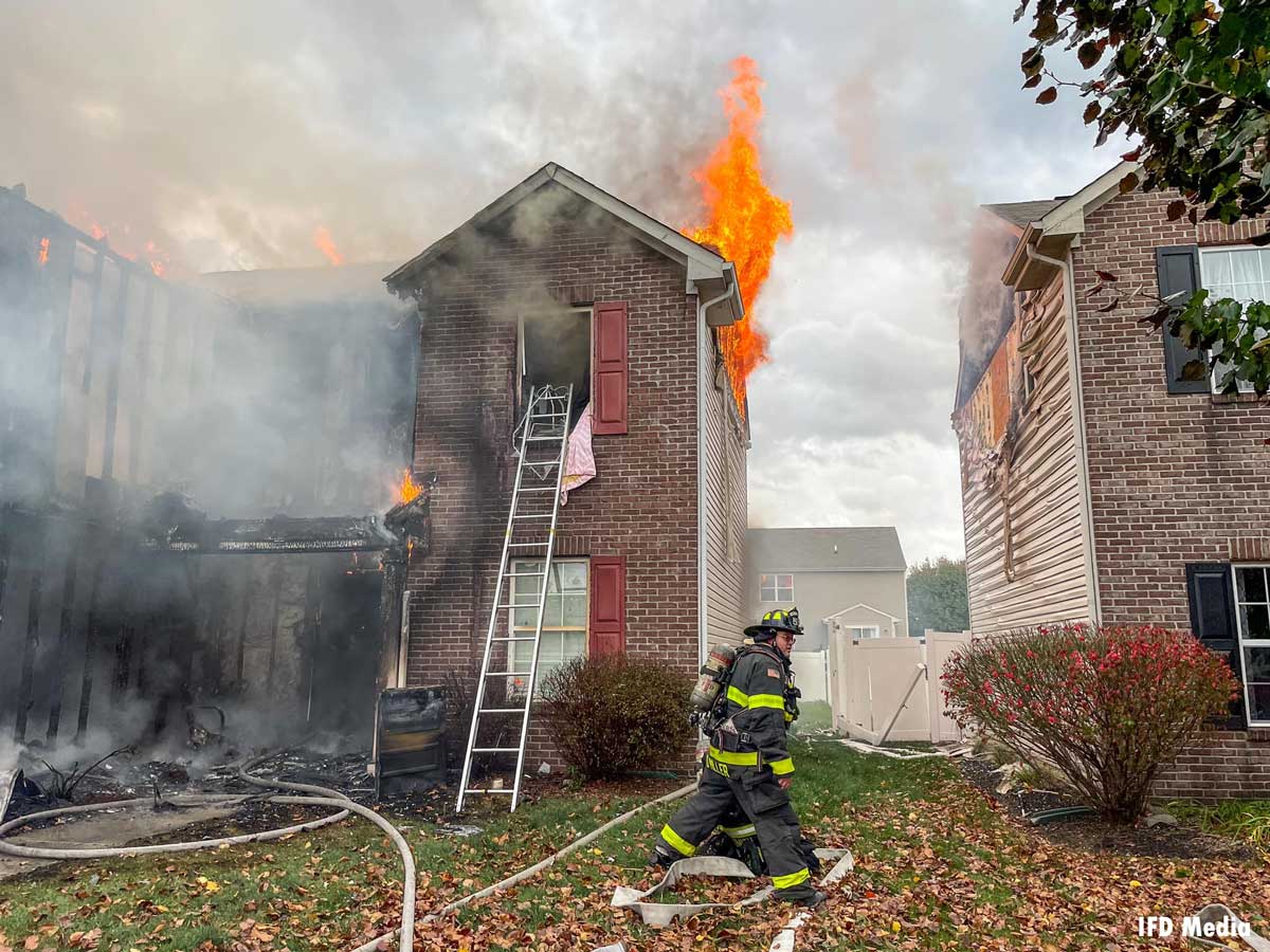 Flames vent from roof of home as Indianapolis firefighter walks by