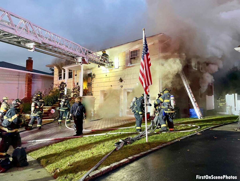 Firefighters deal with hoselines near American flag at Hempstead New York fire