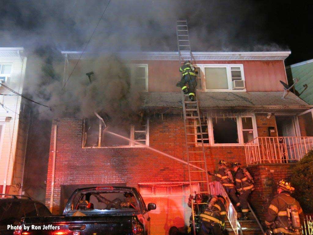 Firefighter ascneds ladder with firefighter putting a stream through window at West New York fire