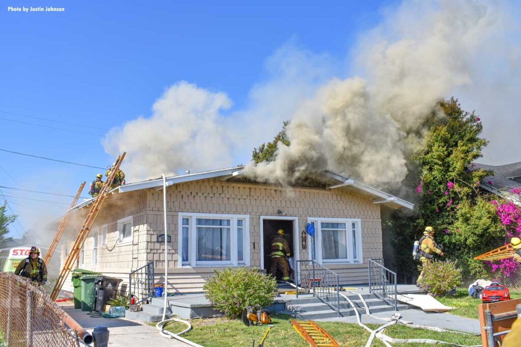 Firefighters at house fire with smoke showing and ladders