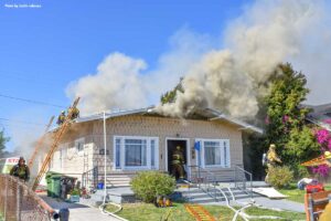 Firefighters at house fire with smoke showing and ladders