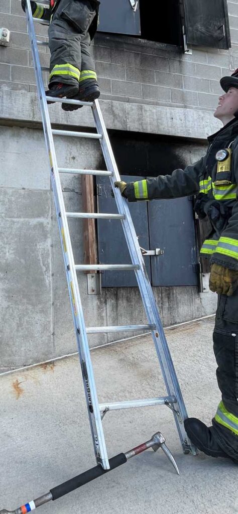 Firefighter holding ground ladder with halligan under spur