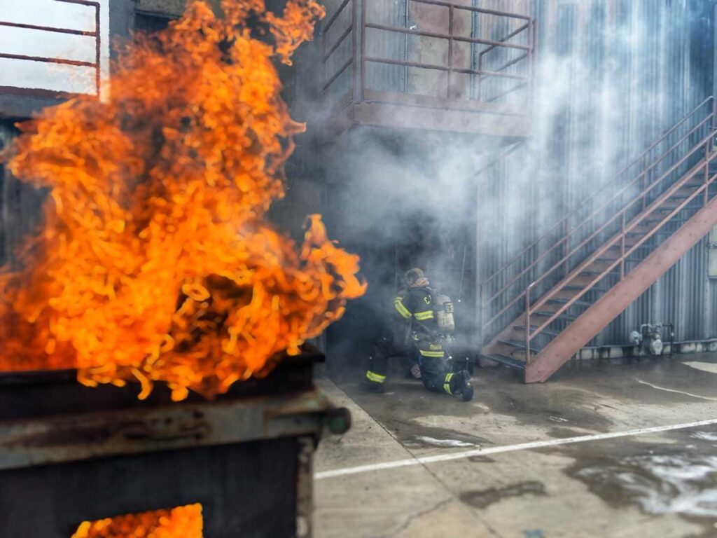 Firefighters undertake training with dumpster against building