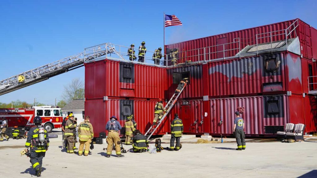 Firefighters climbing ladders at training facility with American flag