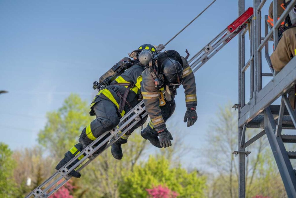 Firefighter holding another firefighter climbing downa portable ladder