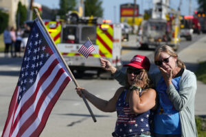 Women with flag and fire trucks at funeral for Corey Comperatore