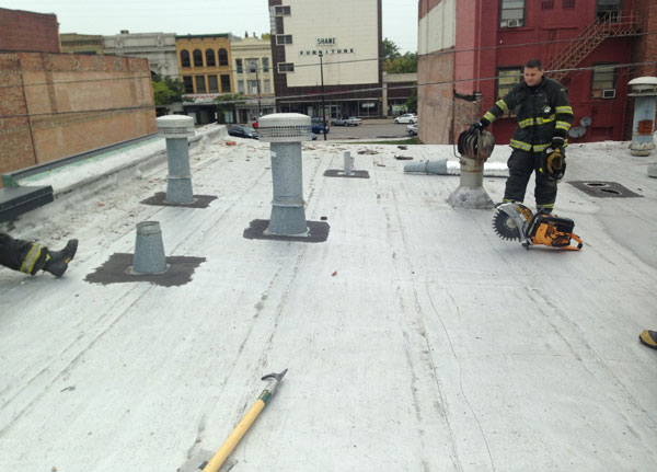 Firefighters with a hoseline and saw on a rooftop.